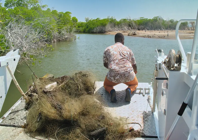 Un homme assis sur un bateau près d’un filet de pêche abandonné.