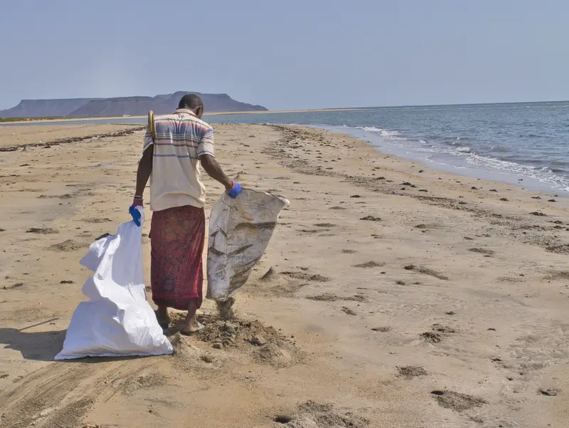 Une personne remplit un sac de déchets sur la plage.