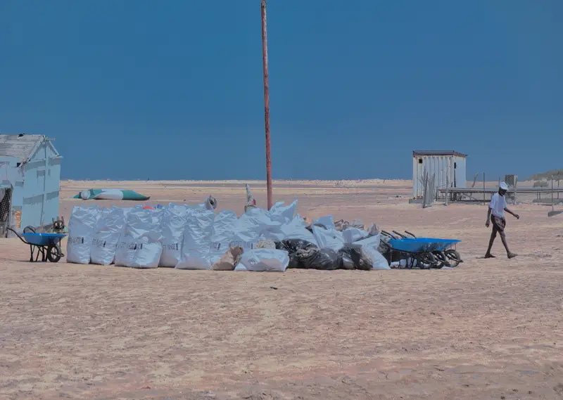Sacs de déchets collectés alignés sur le sable.