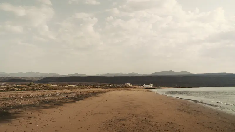 Piste de sable longeant le rivage sous les nuages.
