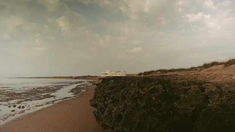 Plage et rochers sombres, un bâtiment au loin.