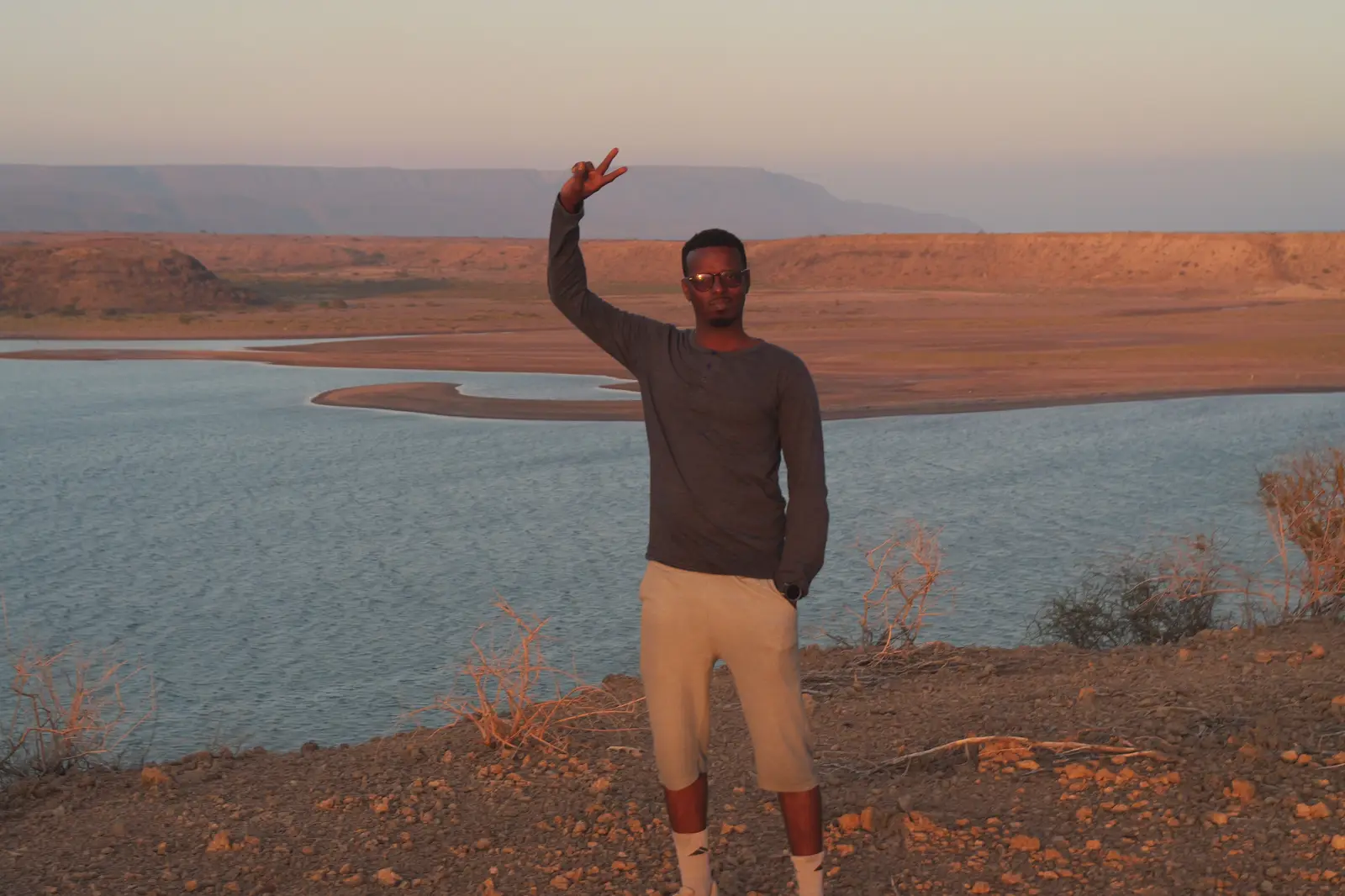 Yacoub Aden Miguil, la main levée, au-dessus de la baie de Raysali au coucher du soleil.