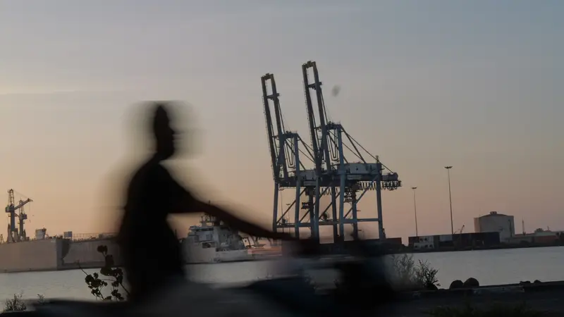 Silhouette floue d’un passant devant les grues du port.