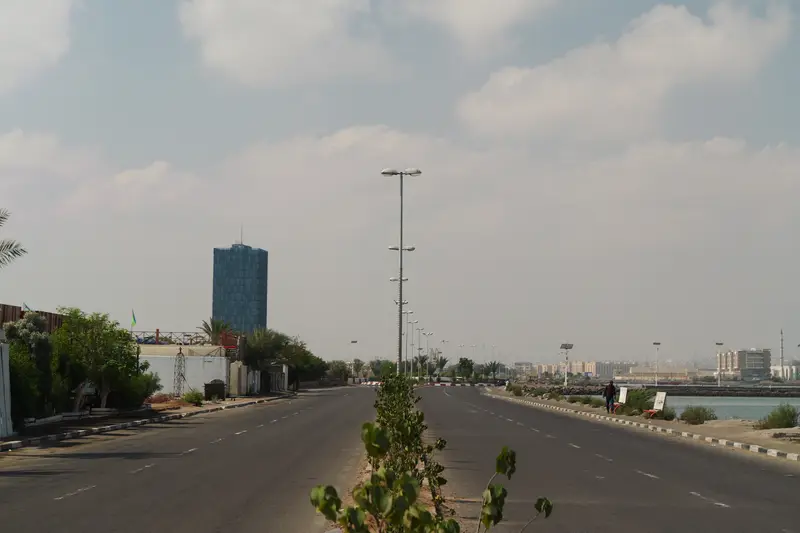 Large avenue vide menant vers une tour, sous un ciel nuageux.